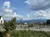 The image depicts a scenic view of a rural landscape with a fenced area, a lamp post, and mountains in the background under a partly cloudy sky.