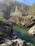 A clear green river winds through a rocky landscape with bare trees and a wooded hillside in the background.
