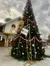 A large Christmas tree decorated with red and silver ornaments stands outside a building adorned with a wreath and a sign labeled 