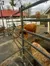 A furry brown cow is standing in a fenced area with hay on the ground.