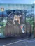 A mural of a bear winking and holding a crushed soda can is painted on a large metal container.