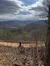 The image depicts a scenic view of a mountainous landscape under a partly cloudy sky, with a leaf-strewn dirt path in the foreground.