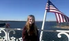 A young person is standing on a deck by the water with an American flag waving in the background.