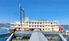 A riverboat with twin smokestacks is docked on a calm, blue lake under a clear sky.