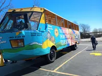 A brightly colored, amphibious tour vehicle is parked in a lot with a person walking away from it.
