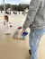 A person in jeans and a gray sweatshirt holds a blue beanbag, preparing to play cornhole on a deck, while a child stands nearby.