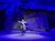 A performer dressed in a cowboy outfit rides a horse in a spotlight against a rocky, blue-lit backdrop.
