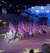 A group of riders on horses carries American flags in an indoor arena, with a backdrop displaying stars and a lit audience area.