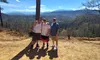 Three men pose happily together on a dirt path with a scenic mountainous backdrop.