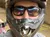 A group of people wearing helmets and goggles are lined up on ATVs, with one person taking a selfie in the foreground.
