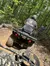Two people are on a muddy trail in a forest, with one riding an ATV and the other standing nearby.