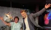 A woman poses with a wax figure of a man, while a wax figure of a woman swinging on a wrecking ball is in the background.