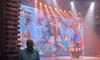 A person stands in front of a stage with bright lights and a large screen displaying a collage of pictures.