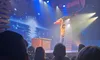 A performer on stage is holding another person overhead as part of an acrobatic act, in front of an audience.