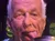 An older man playfully sticks his tongue out while posing behind three jars labeled 