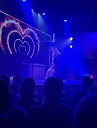 Two acrobats perform a hand-balancing act on stage, with a dramatic light display in the background.