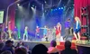 A lively stage performance is taking place with dancers in colorful dresses, accompanied by an attentive audience.