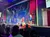 A lively stage performance is taking place with dancers in colorful dresses, accompanied by an attentive audience.