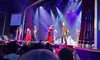 Performers in colorful costumes are on stage during a theatrical show, with an audience watching from the seats.
