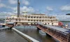 A large, multi-deck paddle steamboat is docked at the pier, with a bridge leading to it under a partly cloudy sky.