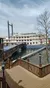 A riverboat with multiple decks is docked alongside a wooden boardwalk under a partially cloudy sky.