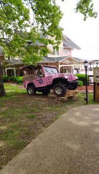 A pink jeep used for tours is parked on a rock in front of a quaint building labeled 