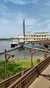 A large riverboat is moored by a wooden walkway on a calm waterfront under a blue sky.