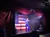 A performer in a blue jumpsuit is singing on stage in front of an American flag backdrop.
