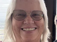Three people are smiling for a selfie indoors with a city view in the background.