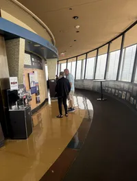 A group of people is standing in an observation deck area with large windows and informational displays.