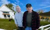 Two people are standing in front of a ranch house with a white fence, under a clear blue sky, with the caption 
