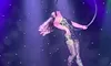 A performer in a shimmering bodysuit is gracefully suspended in the air on a hoop, illuminated by colorful stage lights.