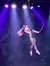 A performer in a shimmering bodysuit is gracefully suspended in the air on a hoop, illuminated by colorful stage lights.