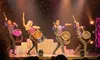 Four performers energetically play large drums on a brightly lit stage with a starry backdrop.