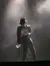 A performer wearing a hat and sparkly glove stands dramatically in a spotlight amidst a smoky background.