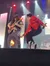 A guitarist in a top hat plays a guitar beside a performer in a red jacket striking a dynamic pose on stage.