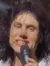 A performer on stage is energetically singing while wearing a black leg brace and surrounded by bright stage lights.