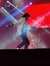 A performer is energetically dancing on stage with dramatic lighting and a drummer in the background.