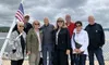 A group of eight people is posing together outdoors on a cloudy day, with an American flag in the background.