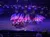 The image shows a group of riders on horses, with glowing attire, carrying American flags in an indoor arena under blue lighting.