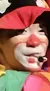 A colorful clown in a vibrant, multicolored costume stands in front of a red curtain.