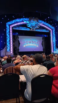 A crowd of people is seated in front of an illuminated stage with a sign reading 