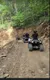 A group of people is riding ATVs on a rugged, dirt trail surrounded by lush green trees.
