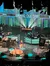 A musician is performing on stage at the Grand Ole Opry with colorful lighting and musical equipment around.
