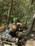 A person wearing a green helmet is riding an ATV on a narrow dirt trail through a forest.