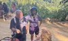 A group of people are gathered around an ATV on a dirt path overlooking a scenic mountainous landscape.