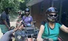 A group of people with helmets are sitting on all-terrain vehicles (ATVs) near a brick building in a wooded area.