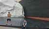 Two people are posing near a large replica of the Titanic with an iceberg, beside a pool of water.