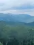 A serene landscape featuring lush green tree-covered mountains under a cloudy sky.