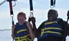 Two people wearing life vests are enjoying a parasailing adventure, each displaying different expressions of excitement.